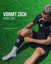 Voetballer trekt de ingebouwde scheenbeschermer over zijn gripsok op het gras