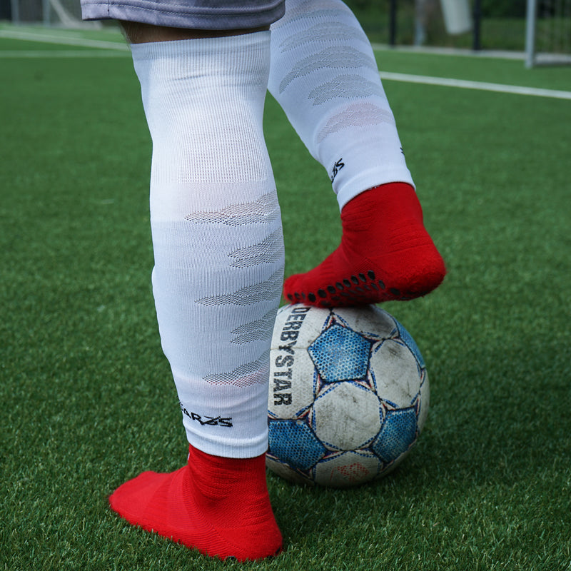 Witte voetbalsokken zonder voet over rode gripsokken op het veld
